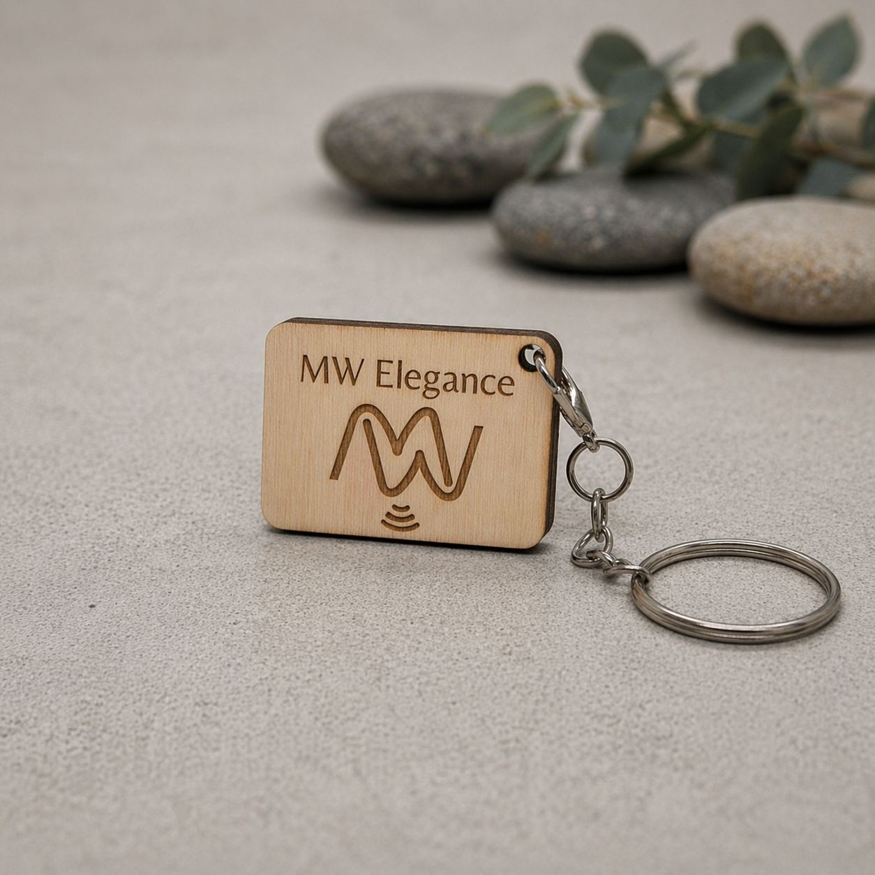 Wooden NFC keychain with 'MW Elegance' branding on a textured surface with stones and leaves in the background.